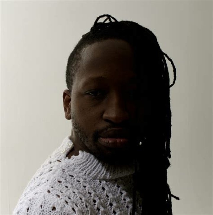 a man with dreadlocks wearing a black hat and scarf over his shoulders