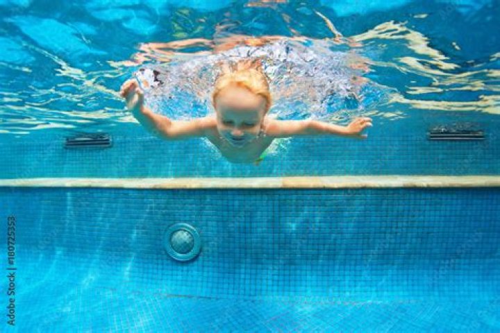 Funny portrait of child learn swimming, diving in blue pool with fun