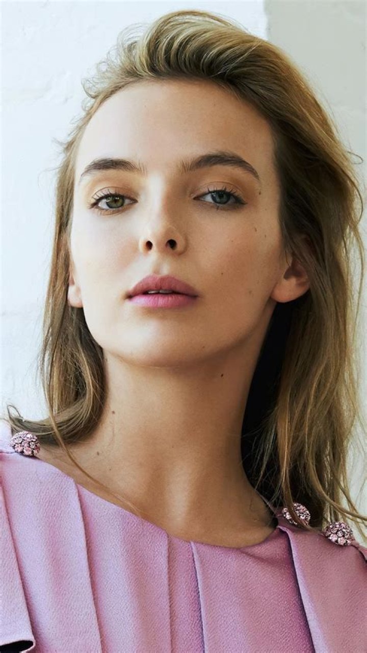 Jodie Comer Is Wearing Light Pink Top With A Background Of White Wall